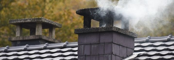 Weißer Rauch aus einem Schornstein auf Hausdach.